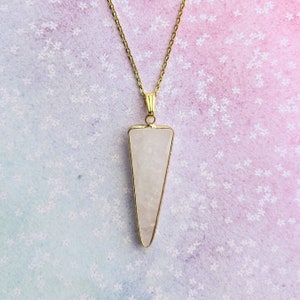 May include: A gold chain necklace with a large, clear quartz pendant shaped like a triangle. The pendant is set in a gold frame.