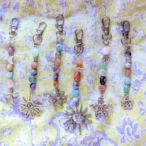 May include: Six silver-toned metal keychains featuring assorted polished gemstone beads in shades of pink, blue, purple, orange, and green. Each keychain includes a lobster clasp and a unique metal charm, including a dragonfly, sun, flower, and star.