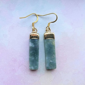 May include: A pair of gold dangle earrings with light blue green stone rectangular pendants.