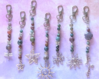 May include: Seven beaded keychains featuring silver-toned lobster clasps and various charms including a dragonfly, stars, a sun, a flower, and a leafy branch. The beads are multi-colored, featuring shades of green, brown, and grey, with silver accents.
