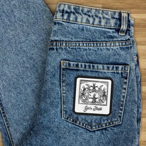 May include: A black and white patch with a graphic of a circle of figures with horns and the text "Circle Eight" in the center. The patch is sewn onto the back pocket of a pair of blue denim jeans.
