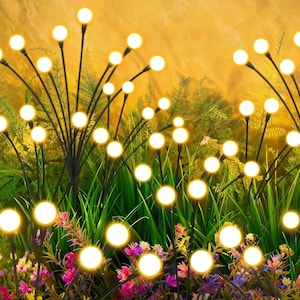 May include: Decorative outdoor solar lights with warm white LED bulbs. The lights are arranged in a garden setting with green grass and colorful flowers. The black stems have multiple bulbs, creating a firefly effect.