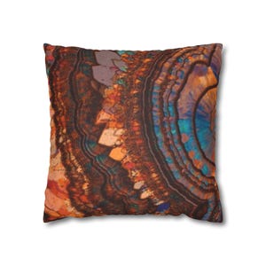 May include: Square throw pillow with a vibrant, abstract design. The pillow features a close-up view of a colorful, layered pattern with shades of brown, orange, blue, and teal. The design resembles a cross-section of a geode or mineral formation.