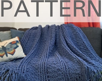 Peut inclure: Une couverture en crochet bleu avec des franges sur les bords. La couverture est pliée et posée sur un canapé.