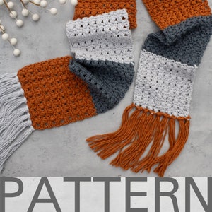 May include: A crocheted scarf with a white, gray, and orange color pattern. The scarf has long fringe on both ends.