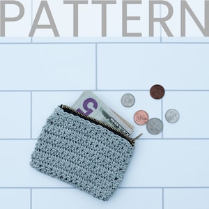May include: A grey crocheted zipped pouch with a zipper pull, cash, and coins inside. The pouch is on a white tiled surface.