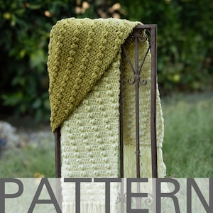 May include: A crochet blanket with a green and white ombre pattern. The blanket is draped over a metal stand and has a fringe border.