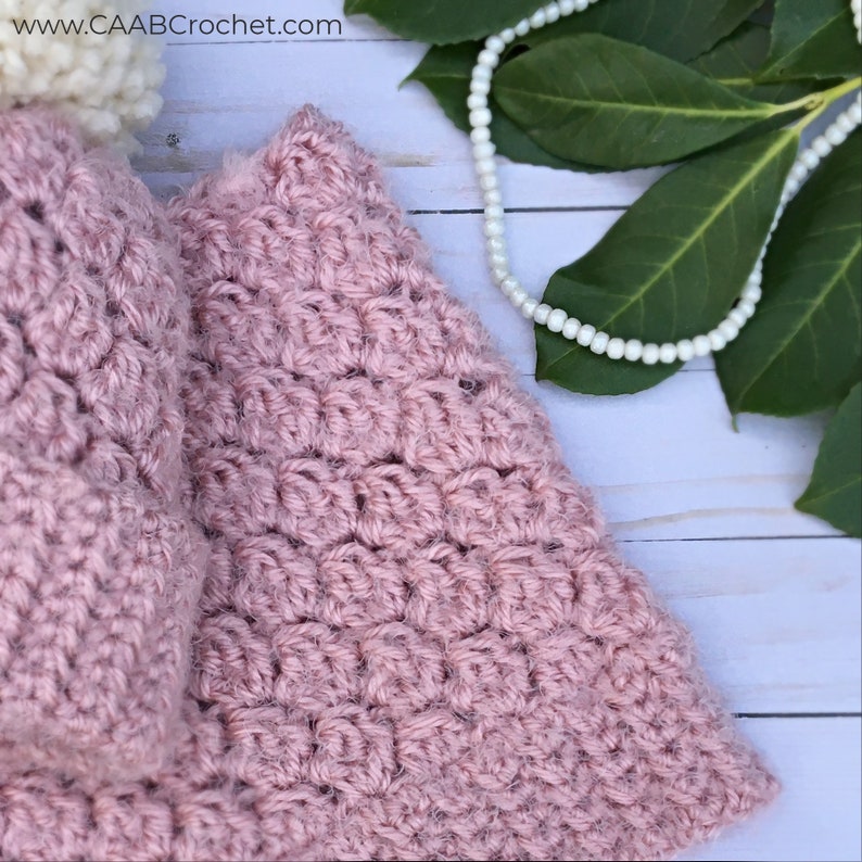 May include: A close-up of a pink crocheted hat with a textured stitch pattern. The hat is made with a soft, fluffy yarn.