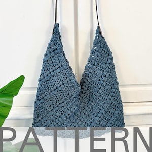 Puede incluir: Un bolso tote azul de crochet con una correa de cuero marrón. El bolso tiene un patrón de puntada texturizado en forma de estrella.