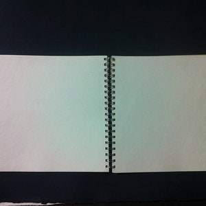 May include: A blank, white, spiral bound notebook with a white cover and a silver binding. The notebook is open to a blank page.