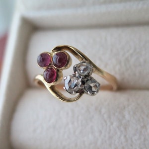 May include: A gold ring with three red gemstones and two clear gemstones. The ring is in a white ring box.