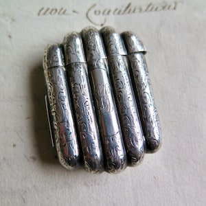 Könnte beinhalten: Eine silberne, gravierte, mehrteilige Pillendose mit floralem Muster.