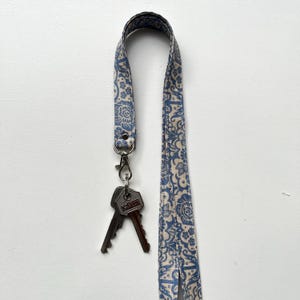 May include: A blue and white patterned lanyard with a silver clasp holding two keys. The lanyard features a repeating floral design. The keys are silver and have a manufacturer's mark.