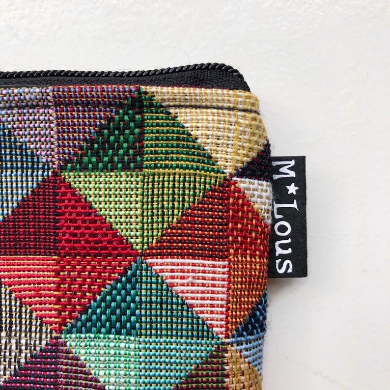 May include: A colorful geometric patterned zippered pouch with a black zipper and a black tag that says "M*LOUS".