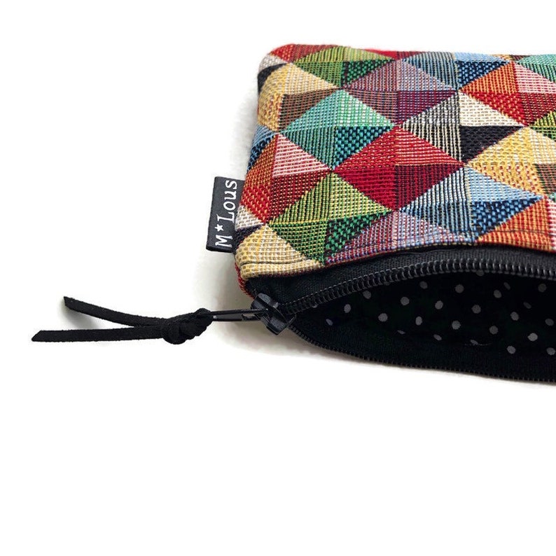 May include: A small zippered pouch with a colorful geometric pattern and a black zipper pull. The pouch has a black lining with white polka dots and a black label with the text "M*Louis".