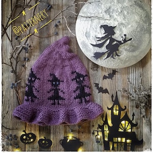 May include: Purple knitted witch hat with black witch silhouettes and a ruffled brim. The hat is on a wooden background with a paper moon, bats, and a haunted house.