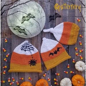 Peut inclure: Trois bonnets en tricot en forme de maïs sucré d'Halloween avec des motifs différents. Un bonnet a une araignée et une toile, un autre a une chauve-souris et le troisième a un simple nœud. Les bonnets sont sur une surface en bois avec du maïs sucré et des citrouilles.