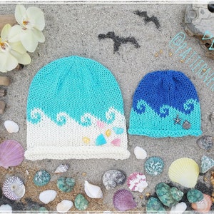 May include: Two knitted hats with a wave design. The larger hat is white and blue with a wave design and seashells. The smaller hat is blue and turquoise with a wave design and a starfish.