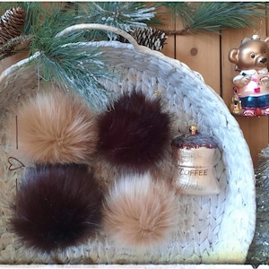 May include: Four faux fur pom poms in a white wicker basket. The pom poms are brown, light brown, and a mix of brown and white.