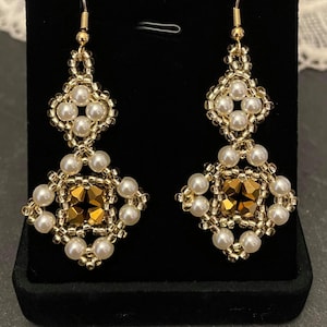 May include: A pair of gold earrings with white pearl beads and a gold crystal in the center of each earring.