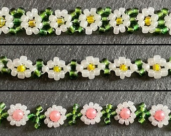 May include: Four beaded daisy chain bracelets. The top bracelet features white and amber beads. The second bracelet has white, green, and yellow beads. The third bracelet has white, green, and yellow beads. The bottom bracelet has pink and green beads.