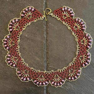 May include: A handcrafted necklace featuring a delicate, openwork design. The necklace is primarily a deep red color, accented with gold-colored beads and a row of purple beads along the scalloped edges. It has a gold-tone clasp.