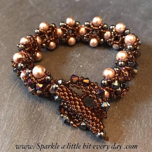 Può includere: Un braccialetto di perline marroni e nere con un ciondolo pendente. Il braccialetto è realizzato con piccole perline marroni e perline nere iridescenti più grandi. Il ciondolo è un design intrecciato con una parte inferiore a punta.