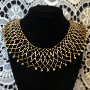 May include: A gold and brown beaded choker necklace with a geometric design. The necklace is on a black mannequin bust.