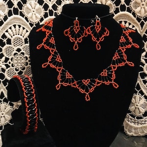 Peut inclure: Un ensemble de bijoux en perles noires et rouges, comprenant un collier, des boucles d'oreilles et un bracelet. Le collier et les boucles d'oreilles sont présentés sur un buste noir, et le bracelet sur un présentoir noir.