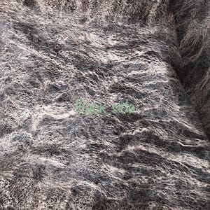 May include: Close-up of a textured fabric in shades of gray, brown, and white. The material has a wavy, almost fur-like appearance, with a mix of light and dark tones creating depth and visual interest. The fabric appears soft and luxurious.