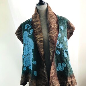 May include: A teal and brown felted vest with a shawl collar. The vest features light blue floral embroidery and a brown trim. The vest is displayed on a mannequin.