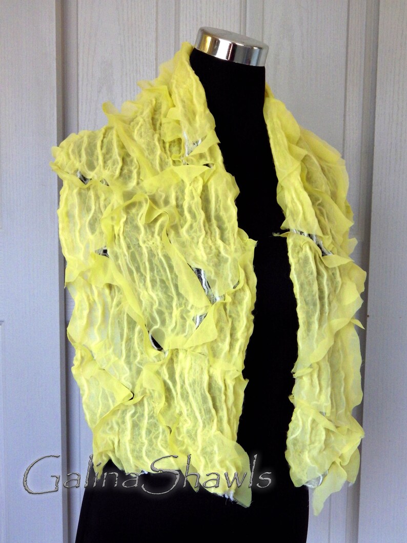 May include: A yellow, ruffled, felted wool shawl. The shawl is draped over a mannequin and has a textured, crinkled appearance.