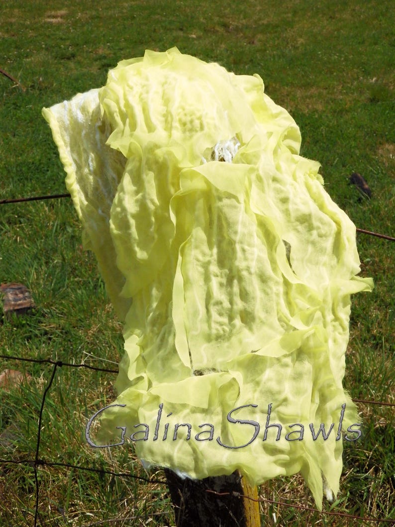 May include: A bright yellow, crinkled, sheer fabric shawl draped over a wooden fence post. The fabric is very light and airy, and it has a delicate, almost translucent quality. The text "Galina Shawls" is visible in the lower right corner of the image.