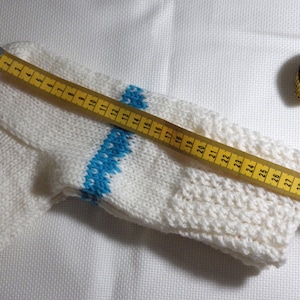 K&ouml;nnte beinhalten: Wei&szlig;e Stricksocke mit einem blauen und wei&szlig;en Streifenmuster, gemessen mit einem gelben Ma&szlig;band. Das Ma&szlig;band zeigt 76 cm an.