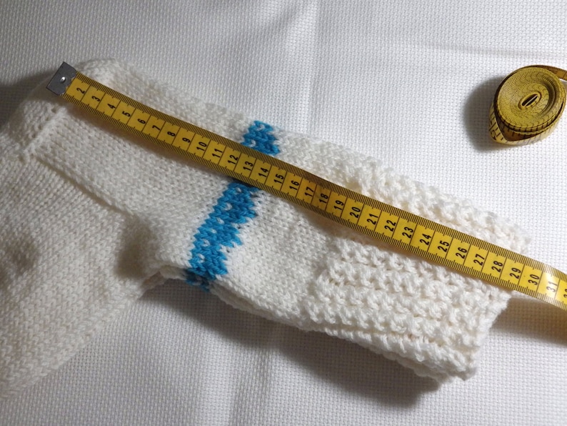 K&ouml;nnte beinhalten: Wei&szlig;e Stricksocke mit einem blauen und wei&szlig;en Streifenmuster, gemessen mit einem gelben Ma&szlig;band. Das Ma&szlig;band zeigt 76 cm an.