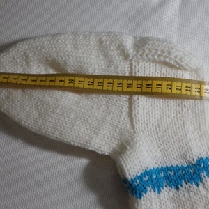 K&ouml;nnte beinhalten: Wei&szlig;e Stricksocke mit einem blauen und wei&szlig;en gemusterten B&uuml;ndchen. Die Socke wird mit einem gelben Ma&szlig;band gemessen, das eine L&auml;nge von 71 cm zeigt.