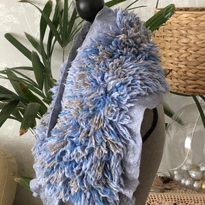 Pode incluir: Uma echarpe de l&atilde; azul claro com um design felpudo e texturizado. A echarpe &eacute; feita de um material macio e confort&aacute;vel e tem uma borda franjada.