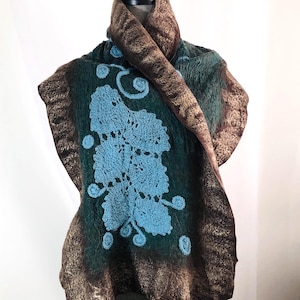 May include: A handcrafted felted wool scarf in shades of green and brown, adorned with a light blue crocheted floral design. The scarf is draped over a mannequin, showcasing its unique texture and artistic detail.