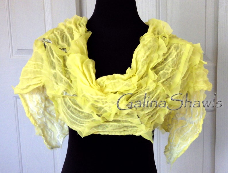 May include: A bright yellow silk scarf with a ruffled texture. The scarf is draped over a black mannequin and has a white, textured design on the edges. The text "Galina Shawls" is visible on the scarf.