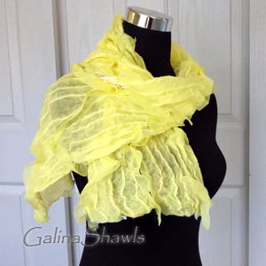 May include: A bright yellow, crinkled silk scarf draped over a black mannequin. The scarf is made of soft, flowing fabric and has a delicate, ruffled texture. The scarf is a beautiful and versatile accessory that can be worn in a variety of ways.