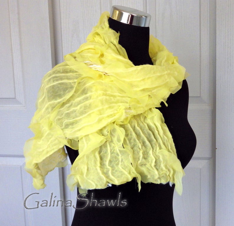 May include: A bright yellow, crinkled silk scarf draped over a black mannequin. The scarf is made of soft, flowing fabric and has a delicate, ruffled texture. The scarf is a beautiful and versatile accessory that can be worn in a variety of ways.
