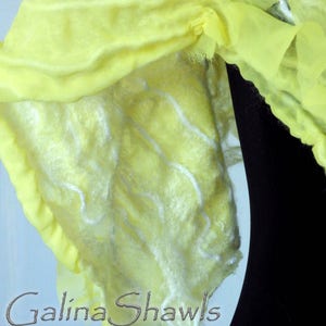 May include: A yellow silk shawl with a white, fluffy texture. The shawl is draped over a black surface and has the text "Galina Shawls" printed on it.