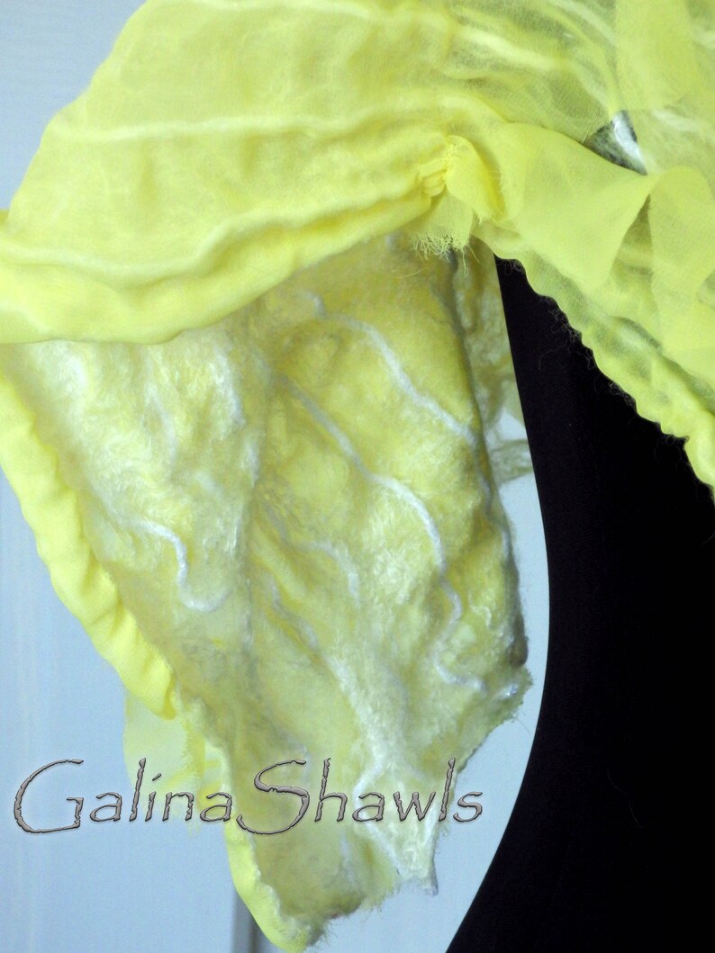 May include: A yellow silk shawl with a white, fluffy texture. The shawl is draped over a black surface and has the text "Galina Shawls" printed on it.