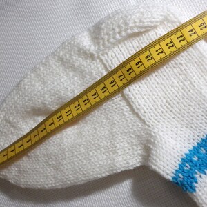 K&ouml;nnte beinhalten: Wei&szlig;er Strickstoff mit einem blauen Streifen und einem gelben Ma&szlig;band. Das Band misst 71 cm.