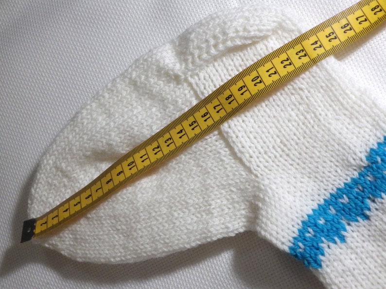 K&ouml;nnte beinhalten: Wei&szlig;er Strickstoff mit einem blauen Streifen und einem gelben Ma&szlig;band. Das Band misst 71 cm.