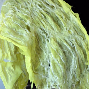 May include: A yellow and white wool shawl with a textured, woven design. The shawl is draped over a black surface. The text "Galina Shawls" is visible in the lower right corner of the image.