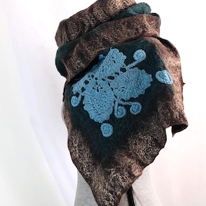 May include: A brown and teal felted scarf with a blue crocheted floral design. The scarf is draped over a mannequin head, showcasing its texture and shape. The scarf's design features a unique blend of colors and textures.