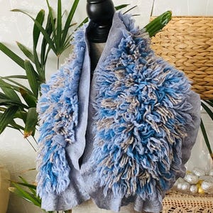 Pode incluir: Um cachecol cinza e azul peludo com um design texturizado e felpudo. O cachecol est&aacute; drapeado sobre um manequim.