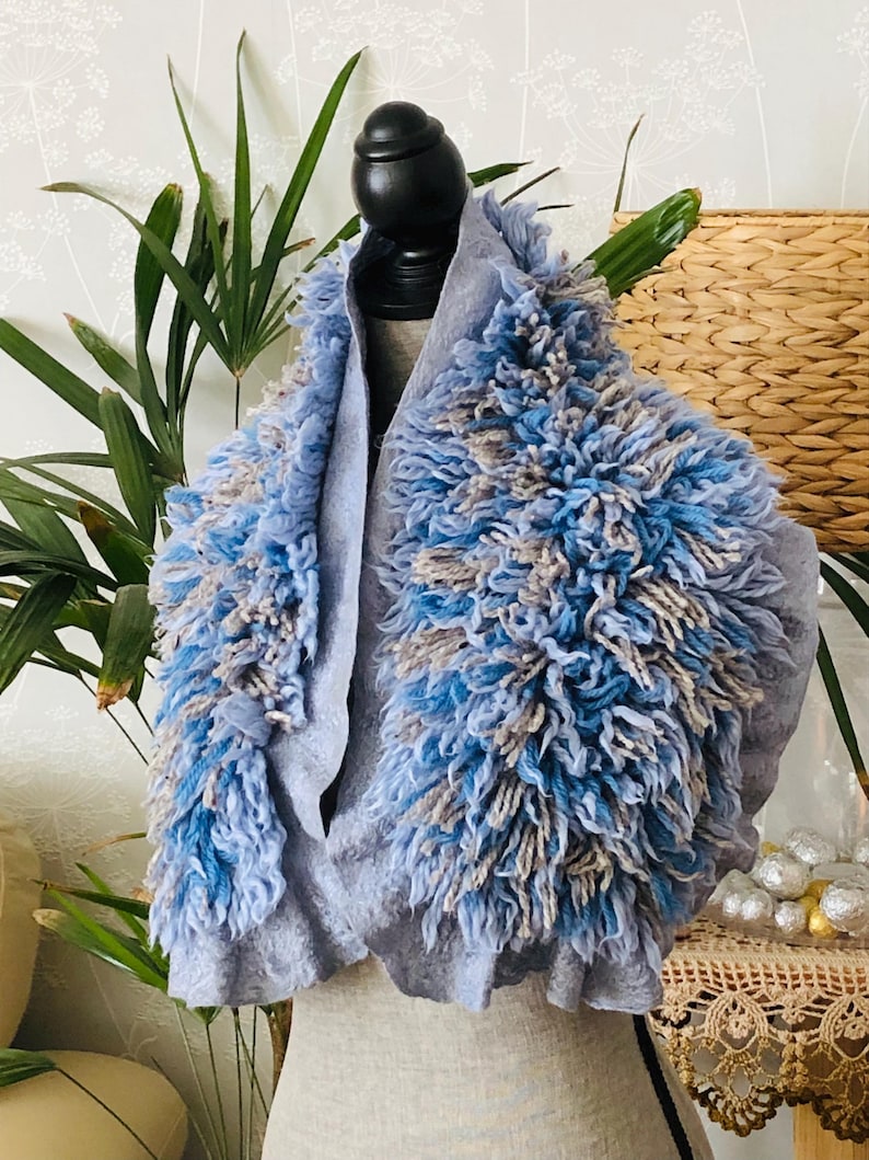 Pode incluir: Um cachecol cinza e azul peludo com um design texturizado e felpudo. O cachecol est&aacute; drapeado sobre um manequim.