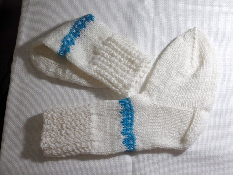 K&ouml;nnte beinhalten: Zwei wei&szlig;e Stricksocken mit blauen Streifen. Eine Socke ist umgeklappt und die andere liegt flach.